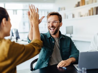 Business people celebrating success in an office Successful business people giving each other a high five in a meeting. Two young business professionals celebrating teamwork in an office.